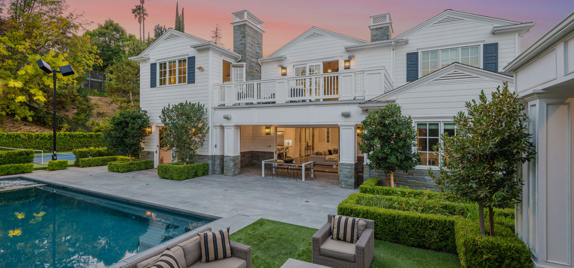 Large two-story house with a swimming pool, set against a backdrop of dusk sky with warm hues.